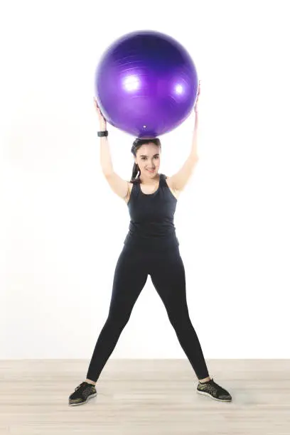 Full length of a pretty Arabian girl workout with a fitness ball while wearing sportswear and smart watch on her hand