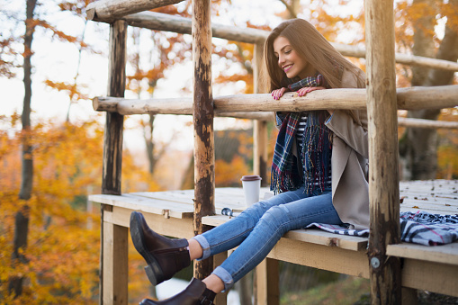 Beautiful young woman sitting on the wooden platform, having fun and enjoying the beautiful autumn environment