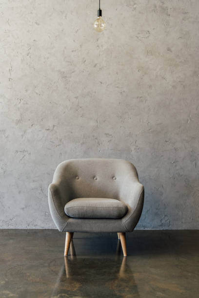istock Cozy modern grey armchair and light bulb hanging in empty room 696170410