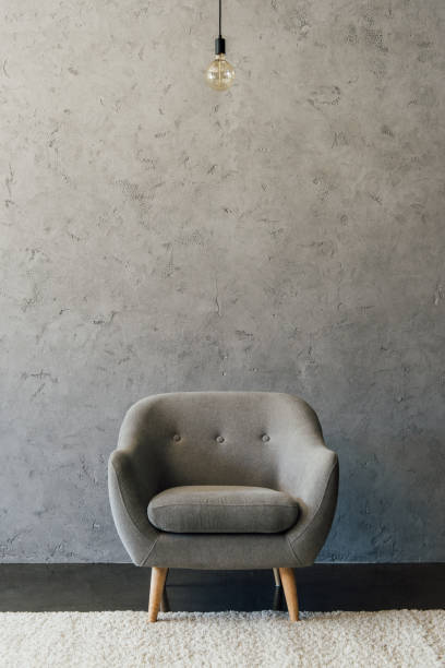 istock Cozy modern grey armchair and light bulb hanging in empty room 696170504