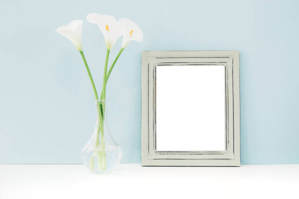 istock Empty wooden frame and flowers in vase on table on blue background. mock up 696174470
