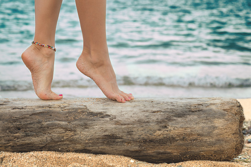 Women's beautiful legs on wooden stump on the beach.