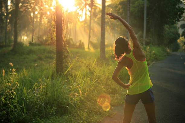 jeune coureur féminin échauffement avant d’exécuter à la piste forestière de matin - joggeuse photos et images de collection