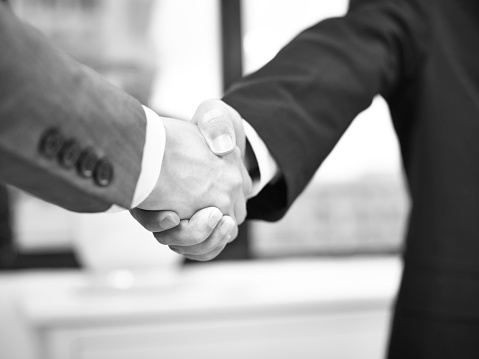 two corporate businessmen shaking hands in office, black and white.