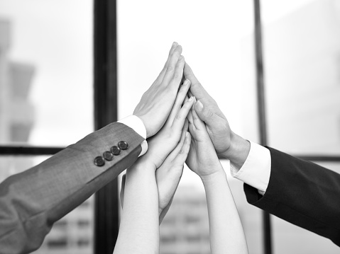 businesspeople putting hands together to form a pyramid in a display of team spirit and determination, black and white.
