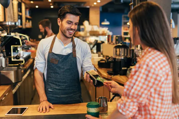 Customer making a contactless payment via credit card at a cafeteria.