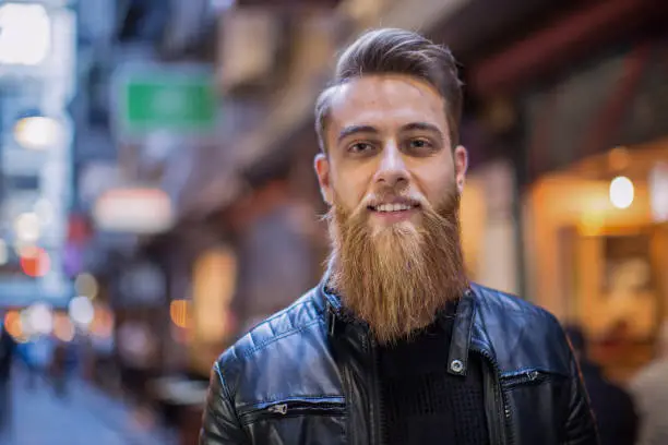 Close up shot of a young man in the laneways of Melbourne, Australia. He has a long beard and is looking at camera