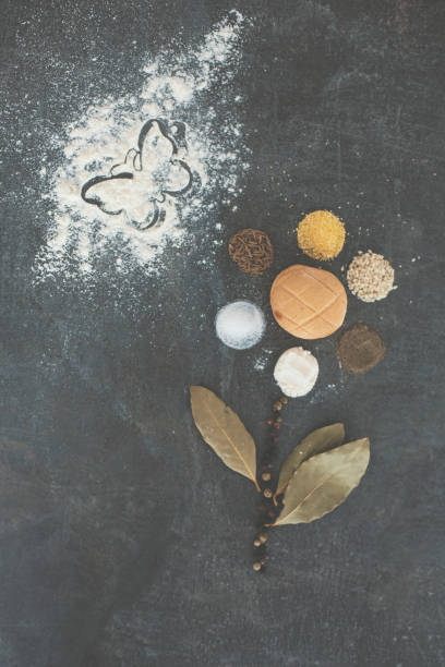 Flower made of food and food ingredients and spices with conceptual butterfly in flour against black wooden background, directly above shot.