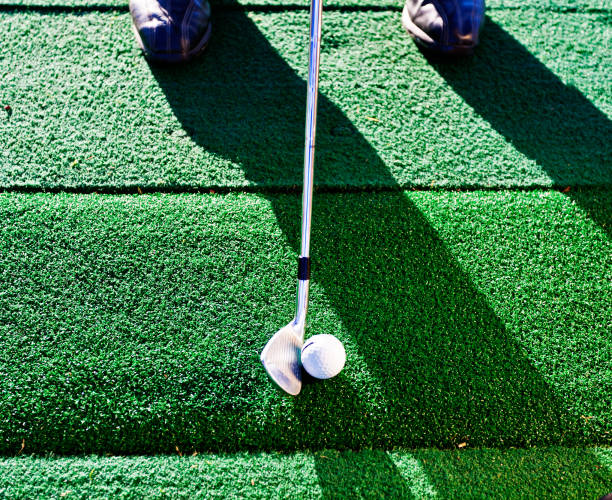 Golf club about to hit ball at driving range Looking down at a golfer's feet as he gets ready to hit the ball on an artificial turf driving range. artifical grass stock pictures, royalty-free photos & images