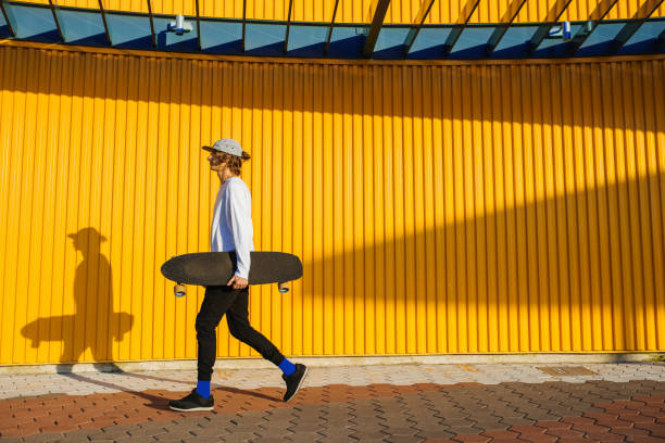 Young skater boy walking outdoors with longboard