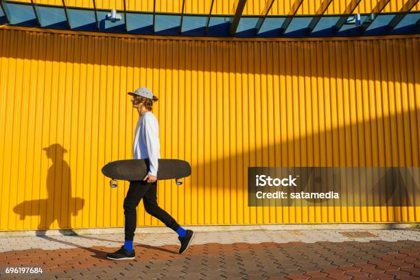 Hipster Teenager Walking With Longboard Stock Photo - Download Image Now - Skateboarding, Multi Colored, Street