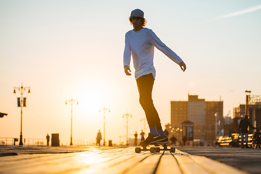 Young skater boy riding longboard on the boardwalk, silhouette on sunset