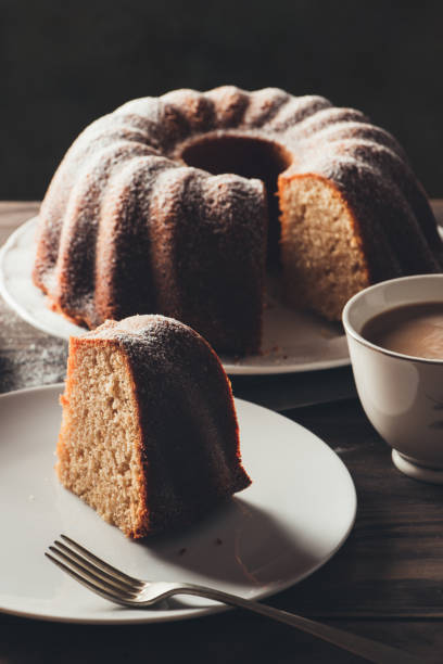 Piece of bundt cake with coffee Slice of yogurt bundt cake served with a cup of coffee with milk. Dark mood sprinkling powdered sugar stock pictures, royalty-free photos & images