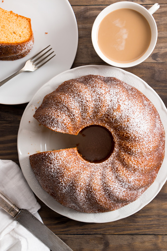 Slice of yogurt bundt cake served with a cup of coffee with milk. Top view