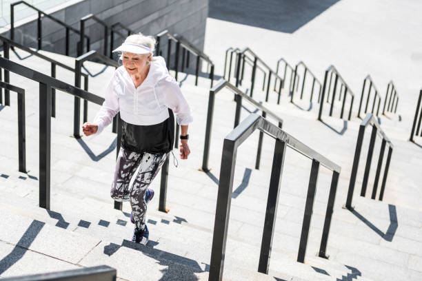 Jolly senior woman practicing cardio exercises outdoors Happy old woman is climbing up city stairs outside. She is smiling and moving ahead. Copy space in right side climbing staircase stock pictures, royalty-free photos & images