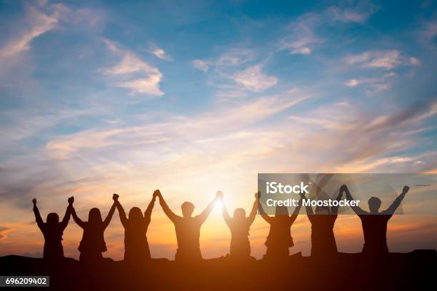 Silueta De Equipo De Negocio Feliz Haciendo Alta Manos En Fondo De Cielo Del Atardecer Por Concepto De Trabajo En Equipo De Negocios Foto de stock y más banco de imágenes de Trabajo en equipo