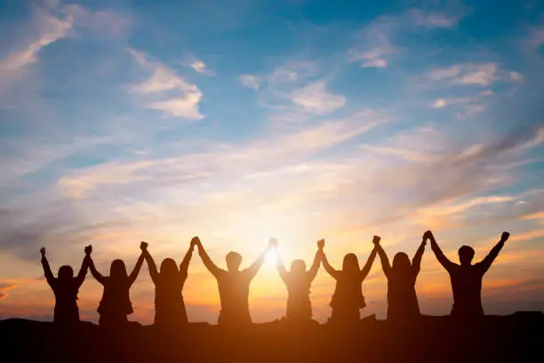 Photo of Silhouette of happy business team making high hands in sunset sky background for business teamwork concept