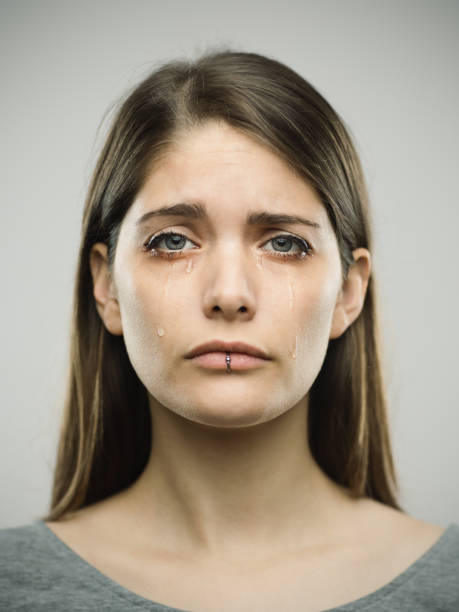 Real young woman crying studio portrait Portrait of sad beautiful young woman crying with real tears. Real people female is against gray background looking at camera. She has long brown hair. Vertical studio photography from a DSLR camera. Sharp focus on eyes. women crying stock pictures, royalty-free photos & images