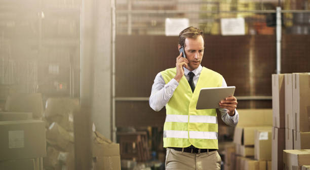 Liaising his next distribution with a client Shot of a man talking on a cellphone while using a digital tablet in a distribution warehouse warehouse office stock pictures, royalty-free photos & images