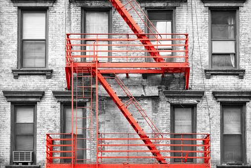 Red fire escape at black and white filtered residential building, New York City, USA.
