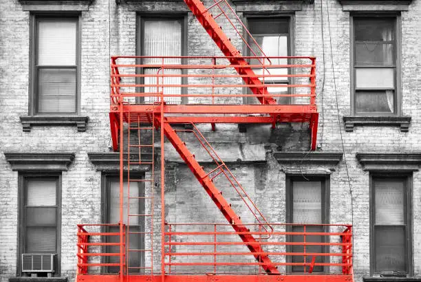 Photo of Red fire escape at black and white filtered residential building, NYC.