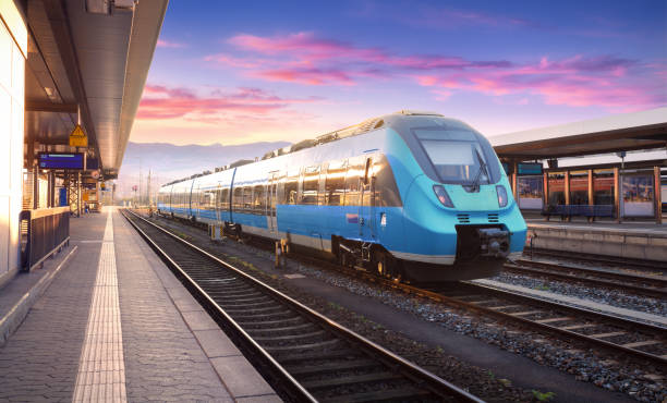 beautiful view with modern commuter train on the railway station and colorful sky with clouds at sunset in europe. industrial landscape with blue train on railway platform. railroad background - transportation railroad track train railroad car imagens e fotografias de stock