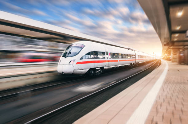 bellissimo treno moderno in movimento sulla stazione ferroviaria al tramonto. treno bianco sui binari della ferrovia con effetto motion blur in europa la sera. piattaforma ferroviaria. paesaggio industriale. turismo ferroviario - treno pendolare foto e immagini stock