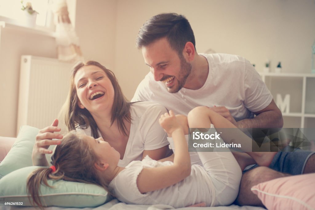 Parents s’amuser avec leur petite fille sur le lit. Famille de passer du temps au matin. - Photo de Famille libre de droits