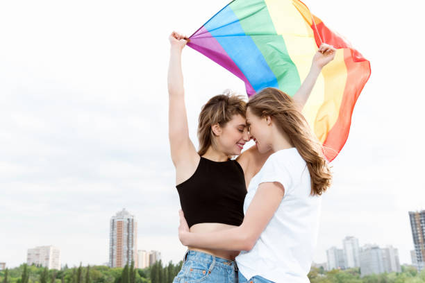 jeune couple de lesbiennes sensuelles embrassant et agitant le drapeau lgbt à l’extérieur - bi sexual photos et images de collection