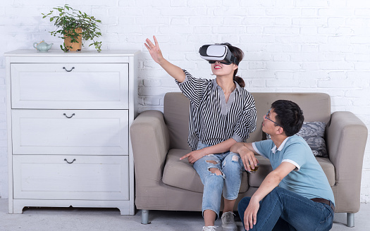 a young Asian couple is experiencing virtual reality headset at home, amazed by this new technology