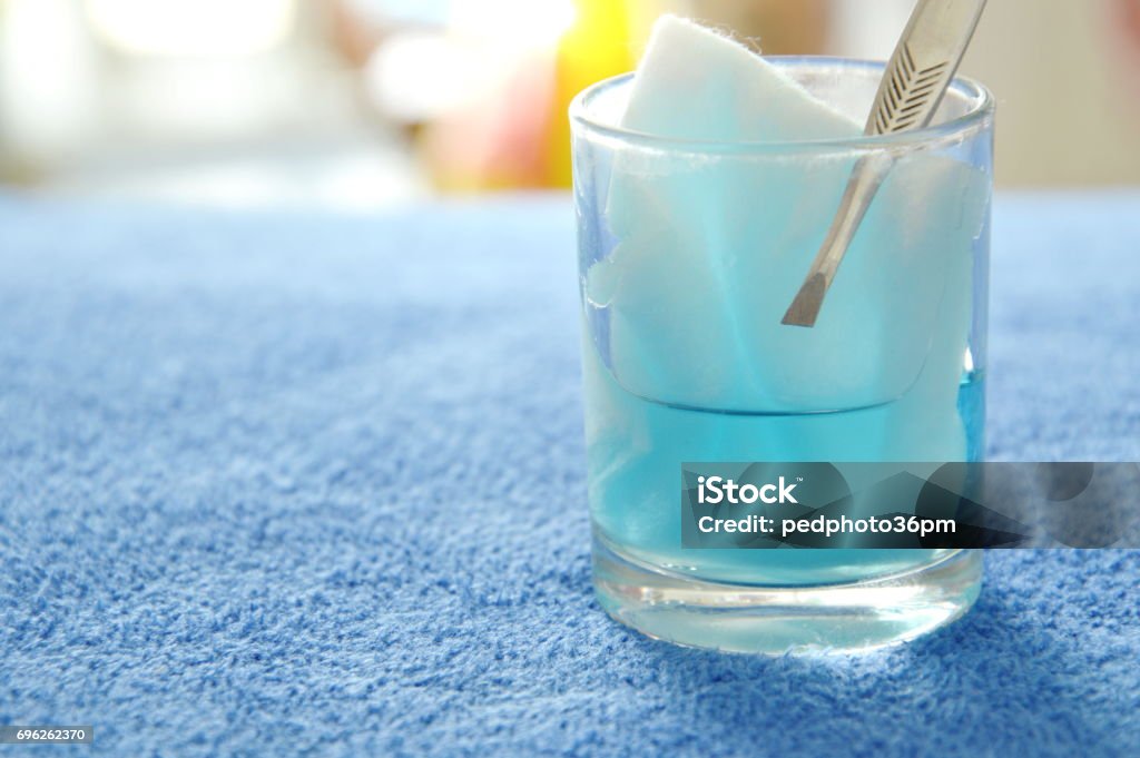 cotton wool with tweezers picking in blue hydrogen peroxide cotton wool with tweezers picking in blue hydrogen peroxide on glass Hydrogen Peroxide Stock Photo