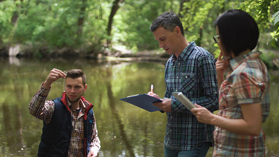 Three ecologists wearing casual clothing exploring lake and taking water sample.