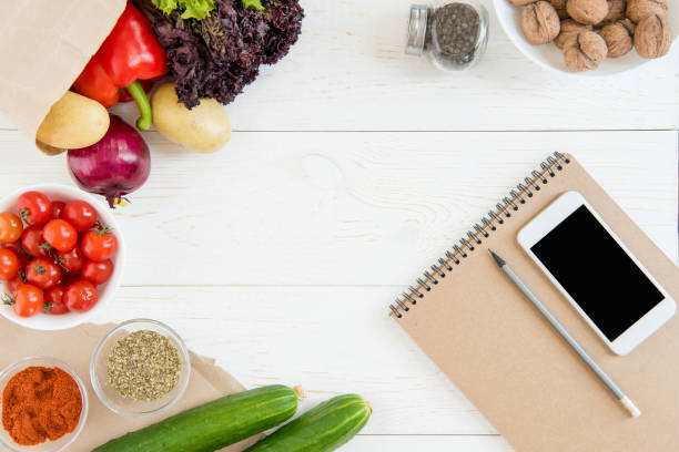 istock Top view of smartphone with blank screen, empty notebook with pencil and fresh ingredients on wooden table 696272720