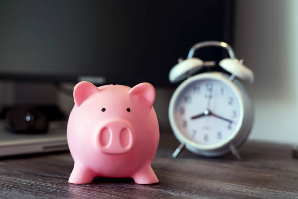 istock Pig money box with clock on a wooden plank 696272886