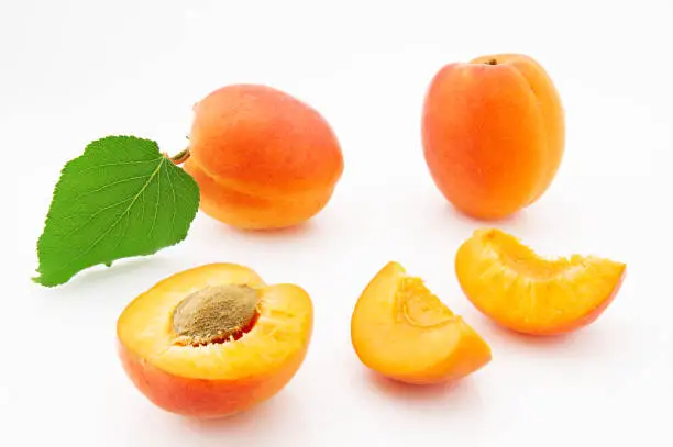 Ripe, juicy and appetizing apricot fruits with green leaves isolated on white background