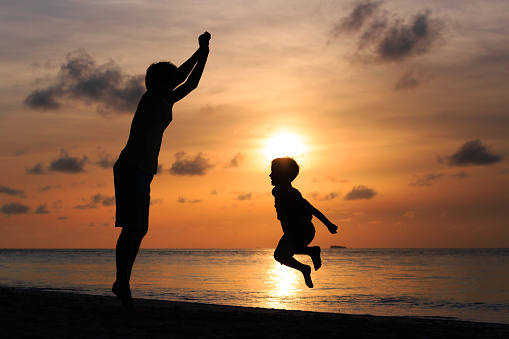 happy father and son jumping at sunset beach, vacation concept