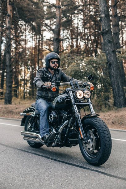 Biker man wearing jeans and leather jacket riding on motorcycle Biker man wearing jeans and leather jacket riding on motorcycle. Forest freedom scene. motorcycle biker stock pictures, royalty-free photos & images