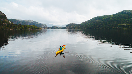 Aerial view of young Caucasian woman kayaking on the lake in mountains, Norway