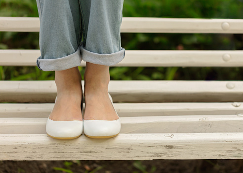 Female legs in blue jeans and white shoes on a white bench. Selective focus.