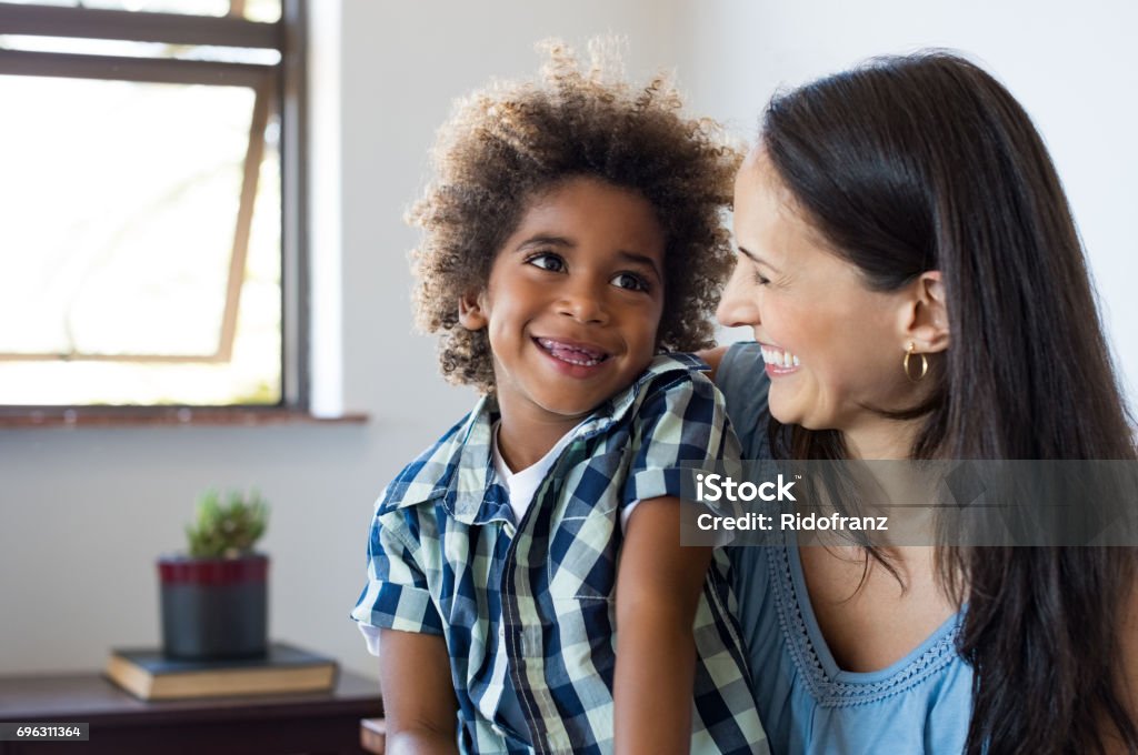 Mother and son laughing Close up face of latin woman playing with her african son. Happy young son feeling loved by mother. Portrait of a lovely mom and cute little black boy looking up at home. Adoption and family concept. Adoption Stock Photo