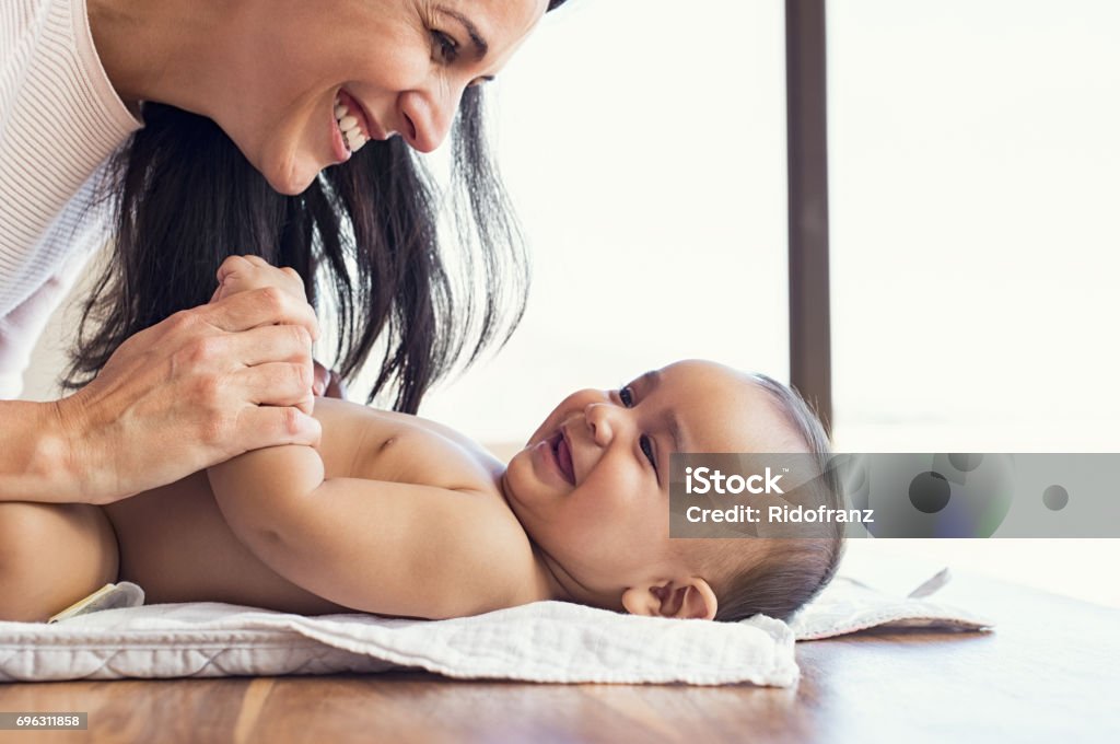 Mother changing diaper to toddler Happy mother playing with baby while changing his diaper. Smiling young woman with baby son on changing table at home. Close up of cheerful mom and toddler boy playing together. Baby - Human Age Stock Photo