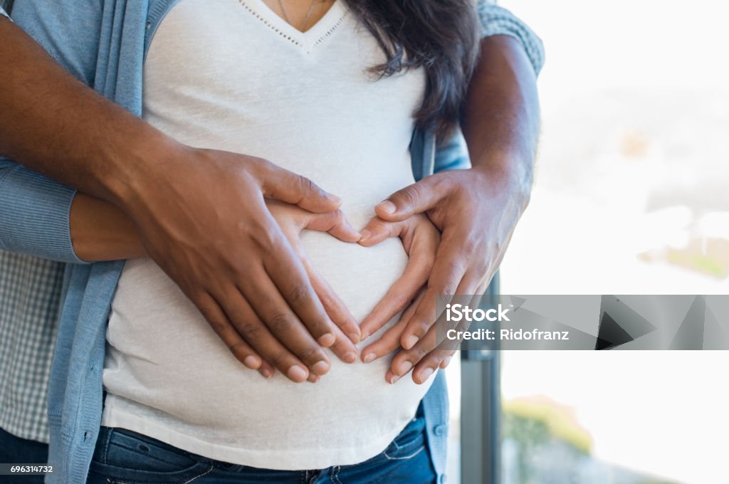 Multiethnic couple expecting a baby Pregnant woman and her african husband holding hand in heart shape on baby bump. Close up of multiethnic couple making heart shape on the tummy. Loving future couple expecting a baby. Pregnant Stock Photo