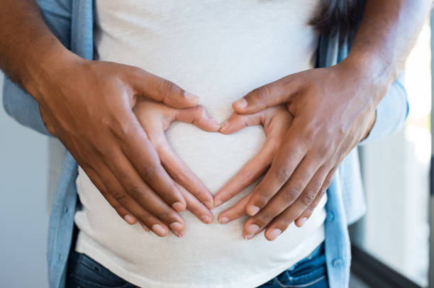 Couple hands on pregnant belly Black man holding belly of his pregnant wife making heart. Pregnant woman and loving husband hugging tummy at home. Heart of hands by multiethnic couple on pregnant belly. heart hands multicultural women stock pictures, royalty-free photos & images