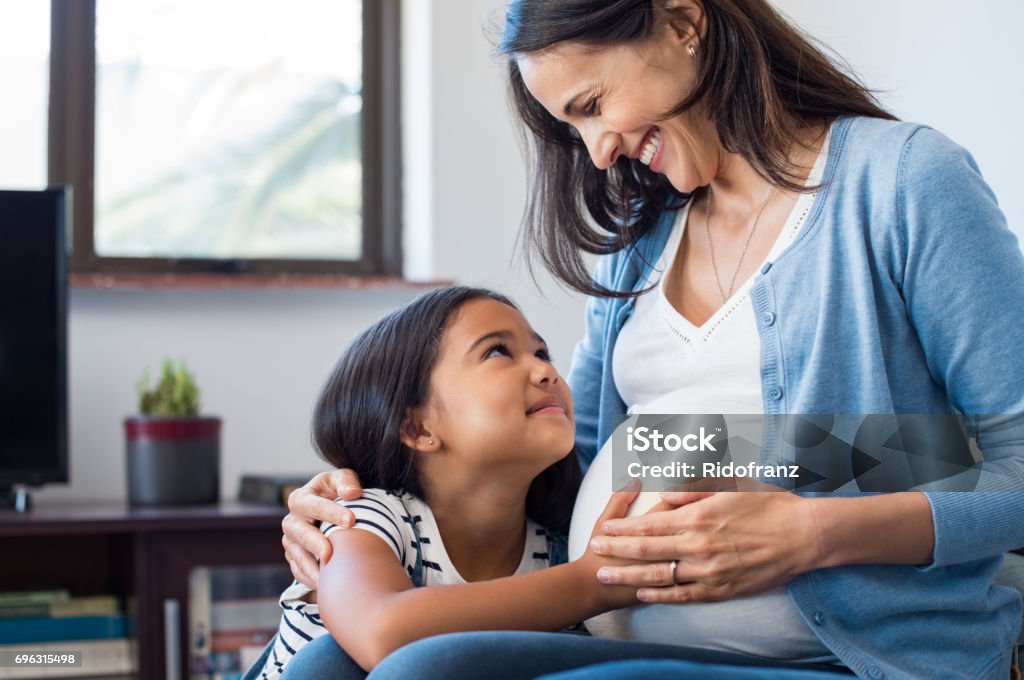 Daughter touching the belly of her pregnant mother Lovely daughter touching mother's pregnant belly. Happy little girl feeling baby at mother tummy and awaiting the birth of her little brother. Pregnant mother relaxing on sofa with her cute daughter. Pregnant Stock Photo