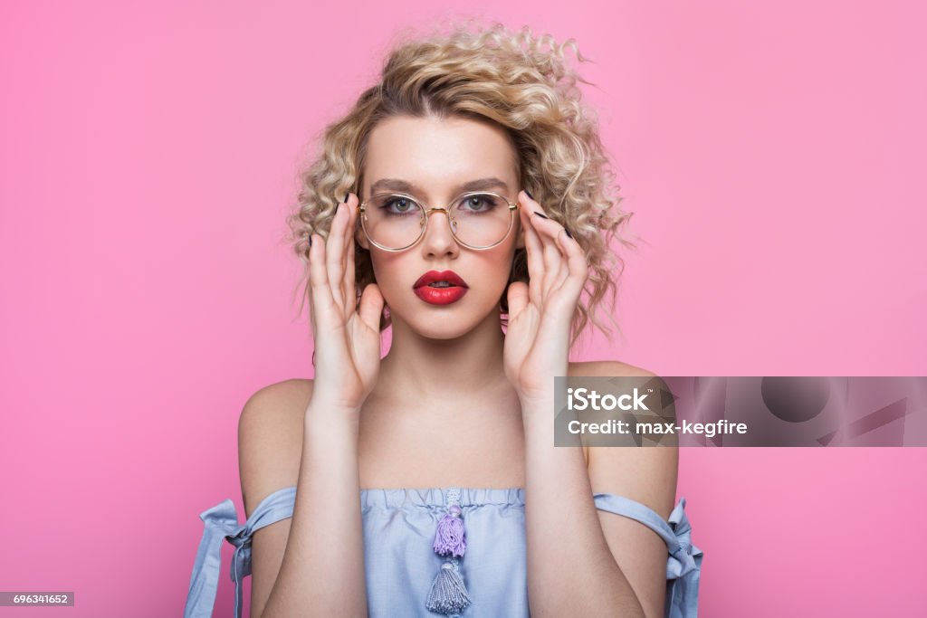 Trendy model looking at camera Portrait of stylish model with curly hair looking at camera on pin background. Eyeglasses Stock Photo