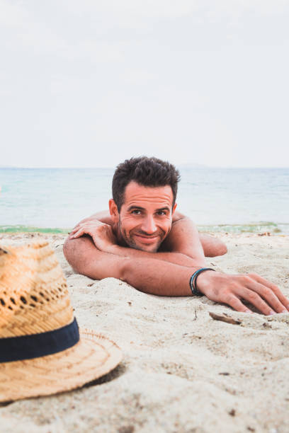 istock Young man on the beach lying in the sand 696346572