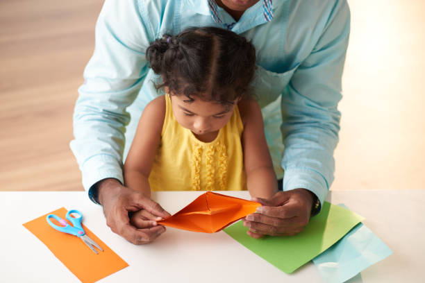 Loving Family Having Fun Together Father spending free time with little daughter: they sitting at table in living room and finishing paper ship, close-up shot toddler hitting stock pictures, royalty-free photos & images