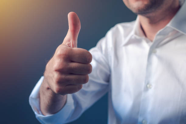 Businessman approving with raised thumb up gesture Businessman approving with raised thumb up gesture, business person in white shirt with roll up sleeves emphasizing approval or satisfaction rolled up sleeves stock pictures, royalty-free photos & images