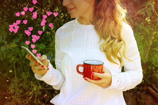 Beautiful happy woman sending love text message on mobile phone with pink hearts