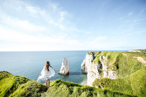 Young woman dressed in hippie style enjoying nature on the rocky coastline with great view on the ocean in France. Wide angle view with copy space